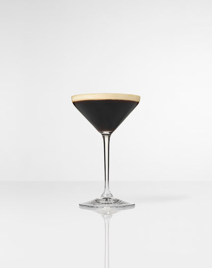 Cocktail glass filled with Espresso Martini, with white foam on top, on a white background.
