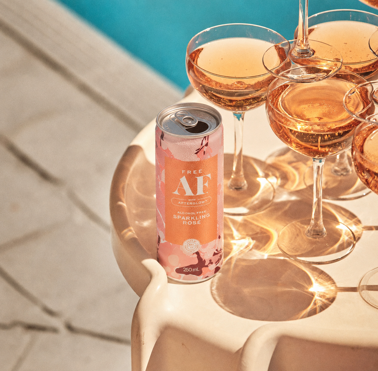 Can of AF sparkling rose next to glasses filled with rose wine by a poolside.